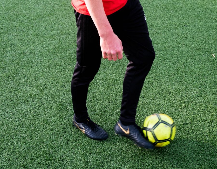 A man kicks a soccer ball on a turf field