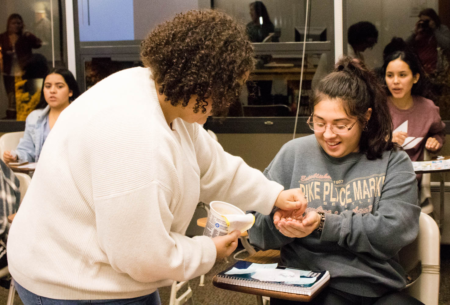 A woman gives a handful of cereal to a seated woman.