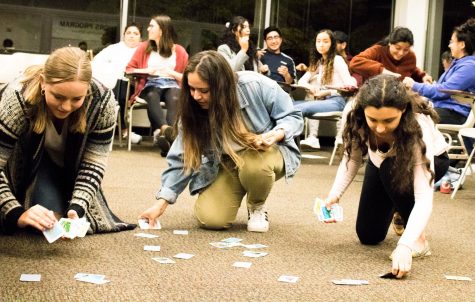 Three women pick up cards off of a floor.