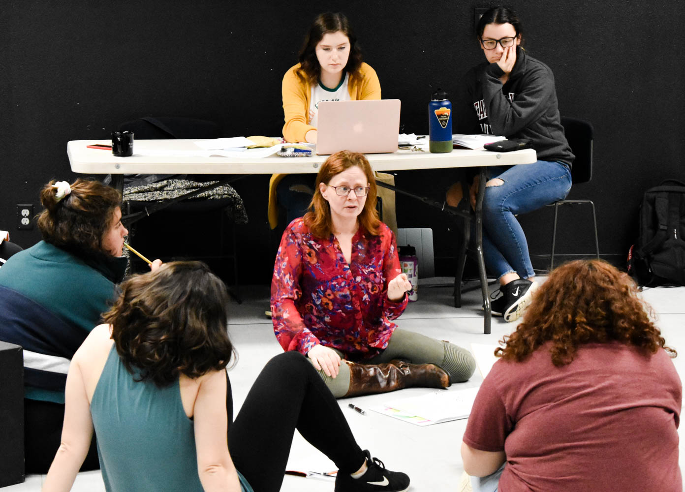 A woman gestures with her hands and speaks to a circle of other people.