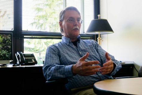 A man sitting at a desk speaking and motioning with his hands