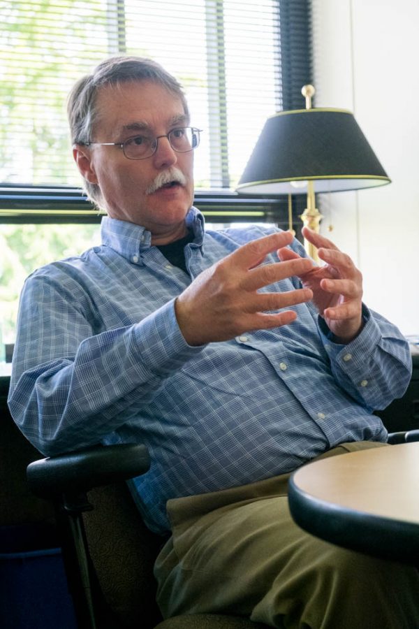 A man sitting at a desk speaking and gesturing with his hands