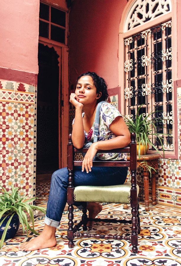 A portrait of Hafsa Bouzekri in a coral painted tiled courtyard.