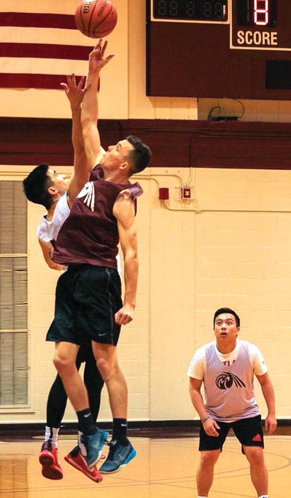 Two men jump in the air to hit a basketball while another player watches.