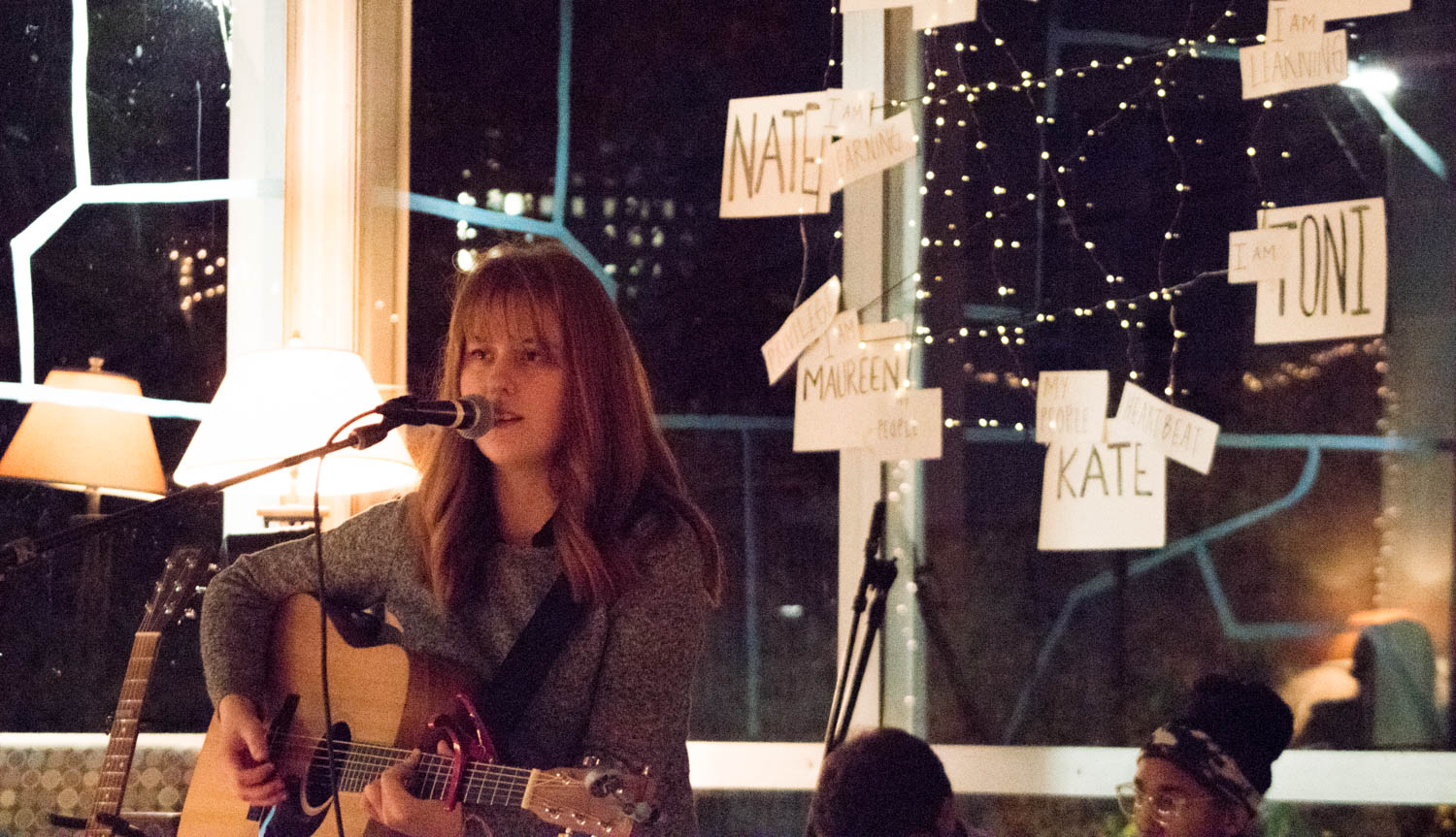 A woman sings into a microphone while playing a guitar