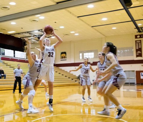 A woman jumps to shoot a basketball while others jump to stop her