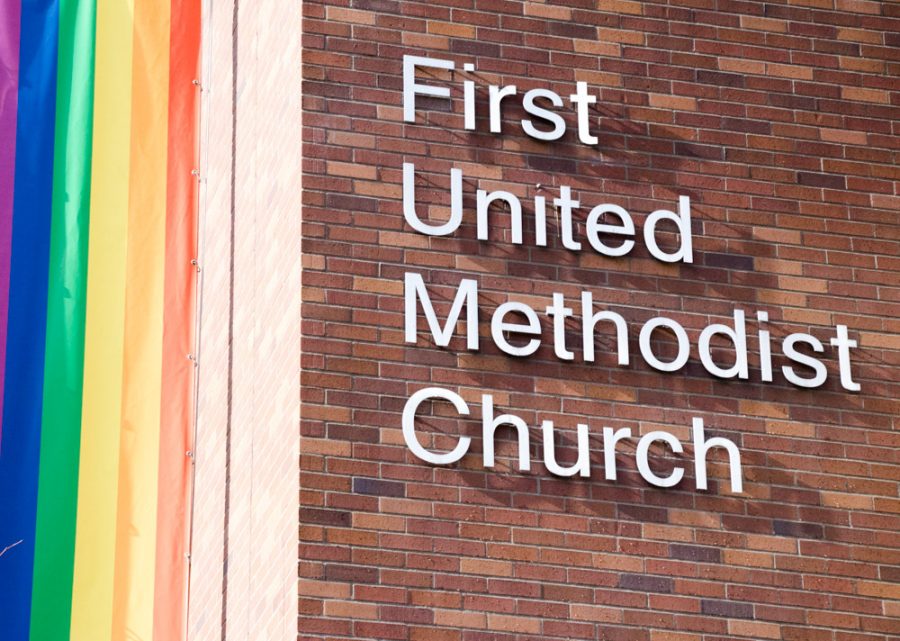 The extorior of a church with a rainbow lgbtq+ flag next to the words First United Methodist Church