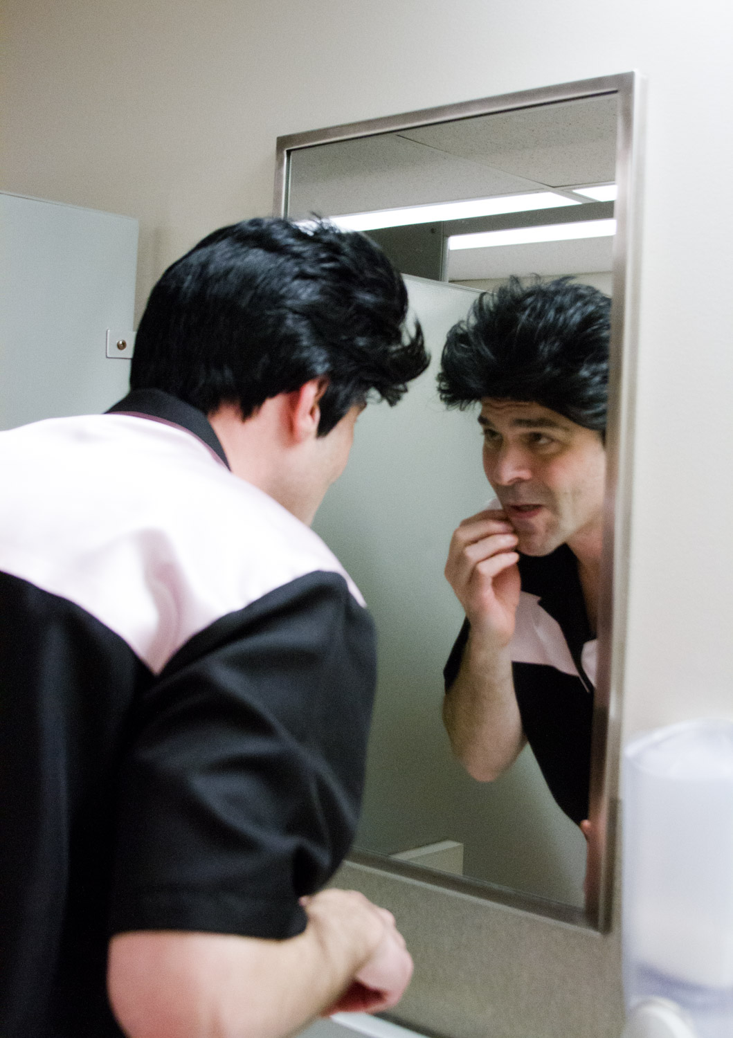 A Elvis tribute artist puts on makeup in a mirror.