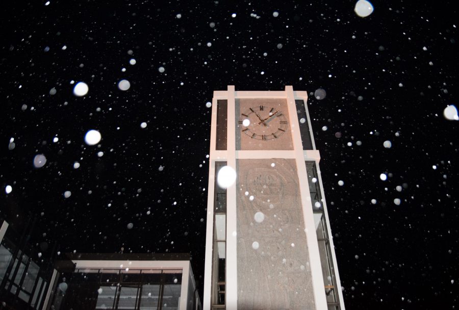 A clocktower is illuminated at night with nowflakes falling around it.