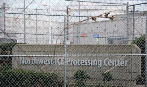 a photos of a sign that reads "Northwest ICE Processing Center" with a chain link fence in front of it