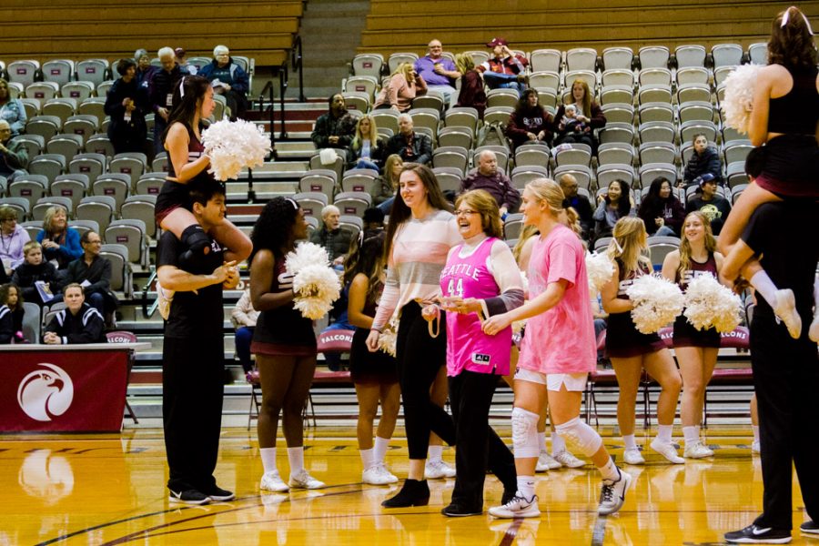 Women in pink shirts walk across the court before a basketball game