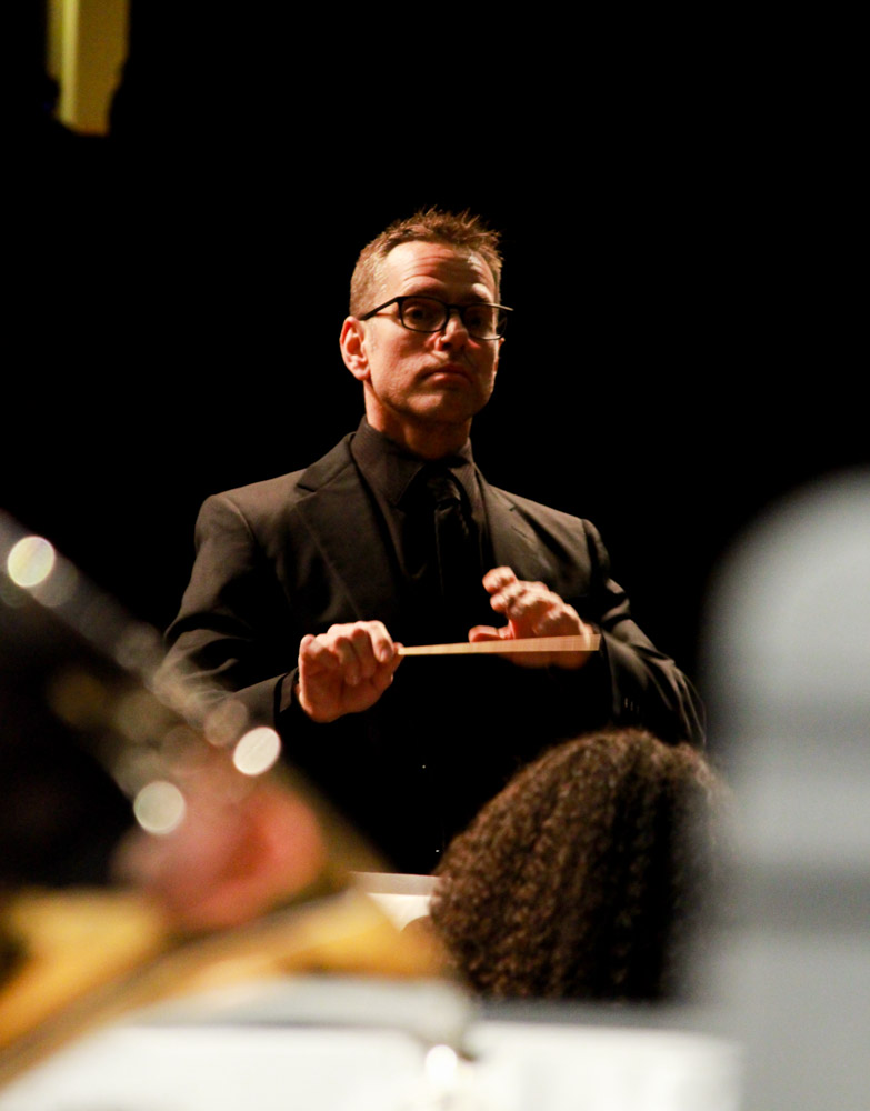 a man stands and conducts musicians