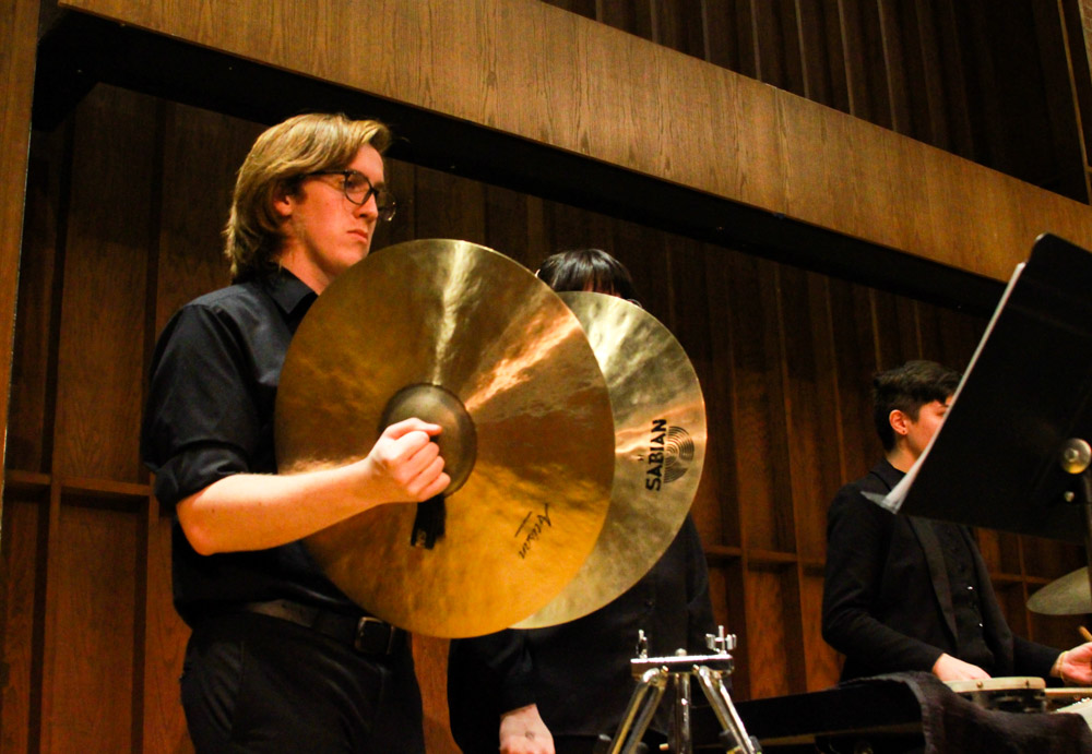 a man stands and holds large cymbals