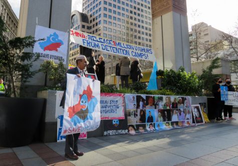 a protester holds a sign that says "#saveuyghur"