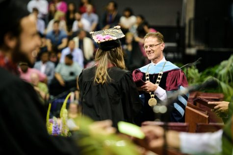 A man wearing academic regalia hands a diploma to a graduate