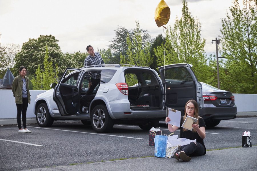 a woman opens birthday gifts in a parking lot as friends watch from a car