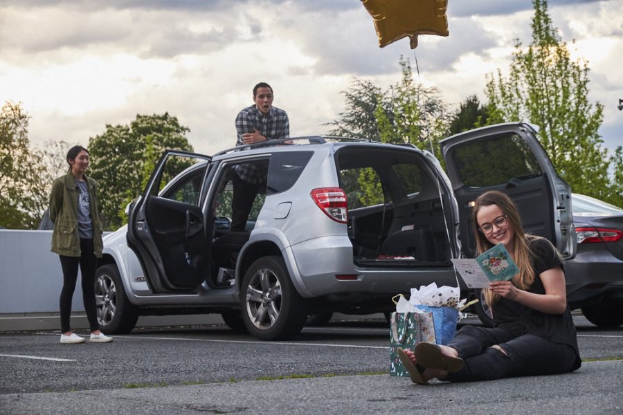 A woman sits in a parking lot and opens birthday presents