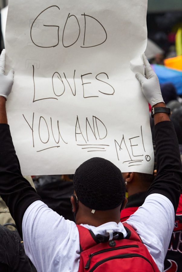 a protestor holds up a sign that reads God loves you and me
