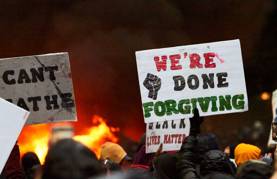 a sign that says were done forgiving is held in the air, with a burning police car in the background