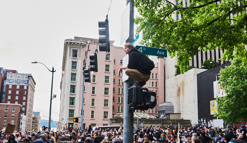A man sits on a stoplight and watches crowds below