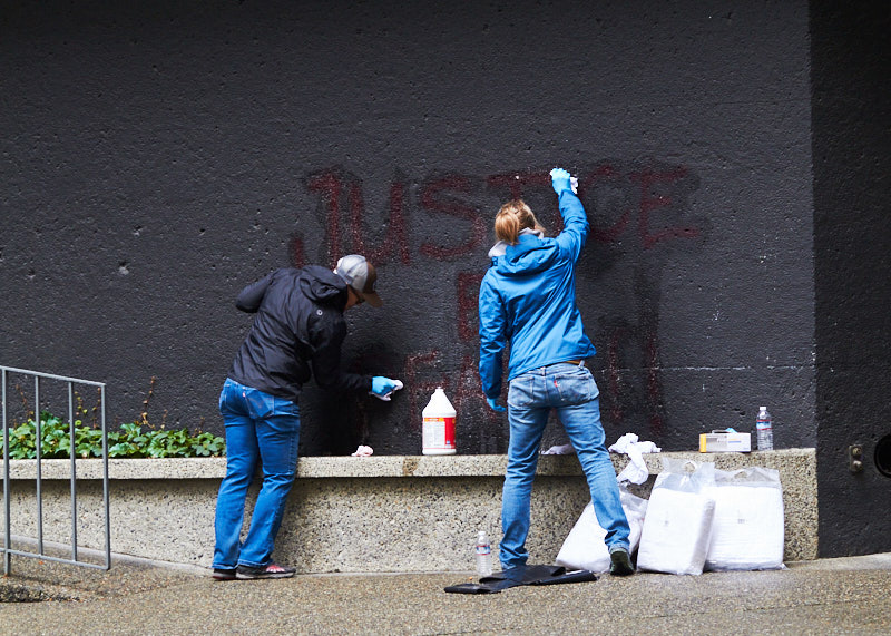 Two people clean graffiti off a wall