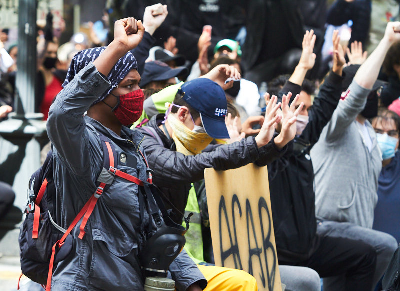 A protestor kneels on the ground with a fist in the air
