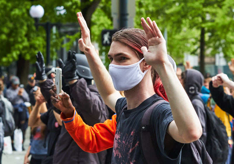 a protestors stares at police with his hands in the air