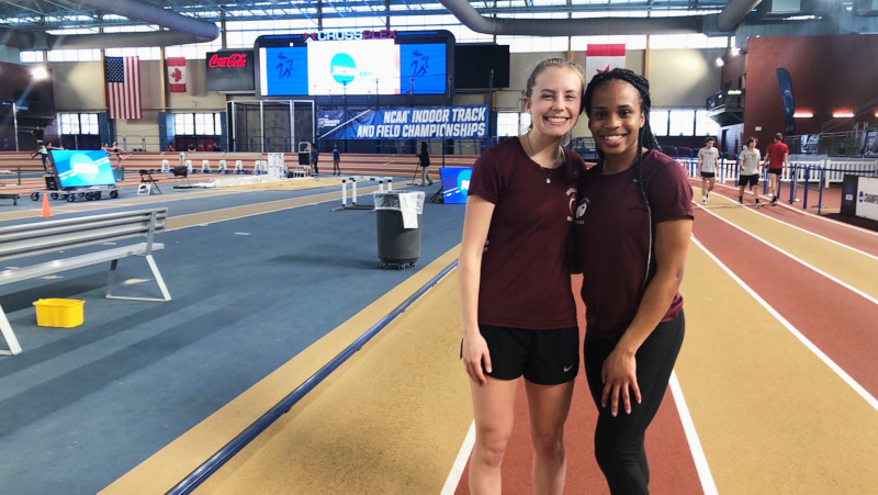 two female athletes pose for a photo on an indoor track