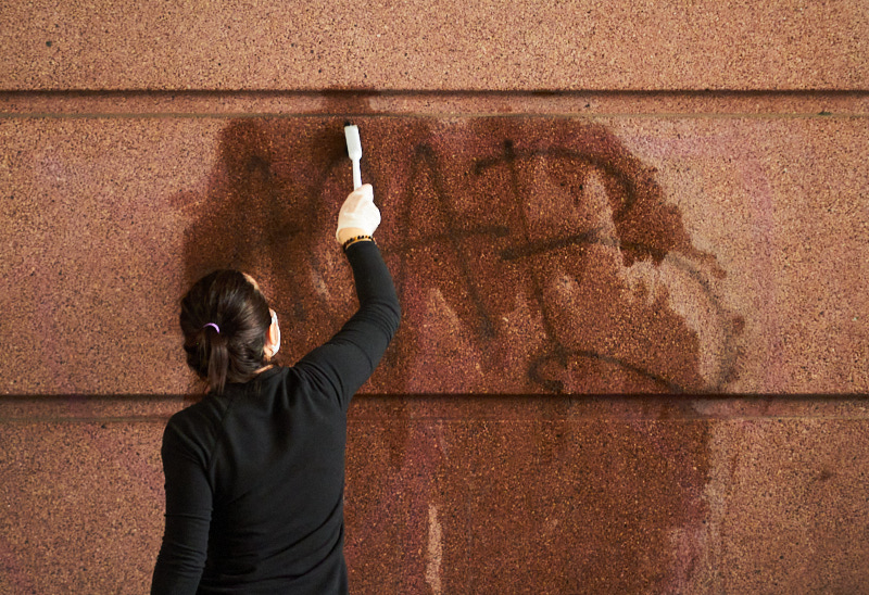 A woman scrubs graffiti off a wall with a brush