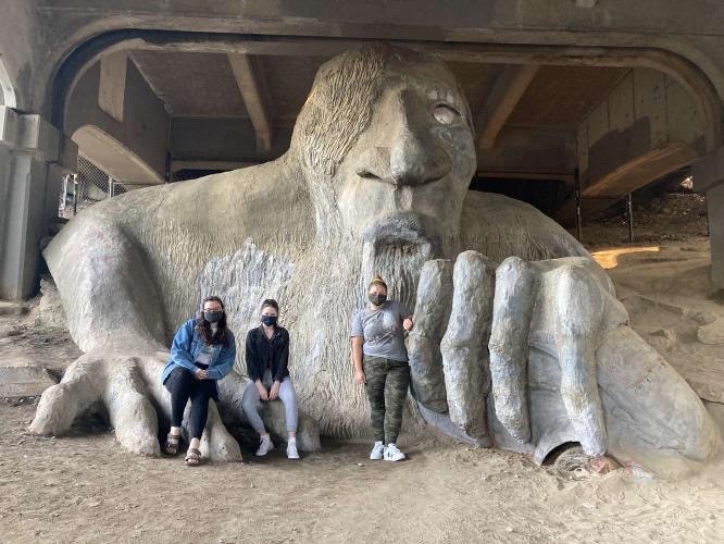 Megan Nixon, Lydia Porter, and Lexi Poisel (from left to right) take a photo with the Fremont Troll for SPUs scavenger hunt.