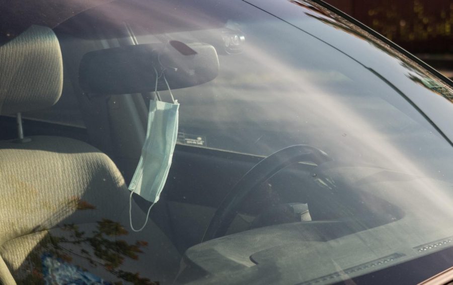 A face mask hangs from the mirror inside a car.