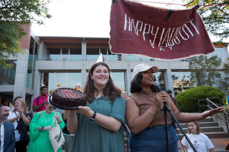 Cambria Judd-Babbitt presents a cake with the writing happy lawsuit day printed on it as Reena Sidhu addresses the crowd gathered in Martin Square at Seattle Pacific University In Seattle, Wash., on Sept. 12, 2022.