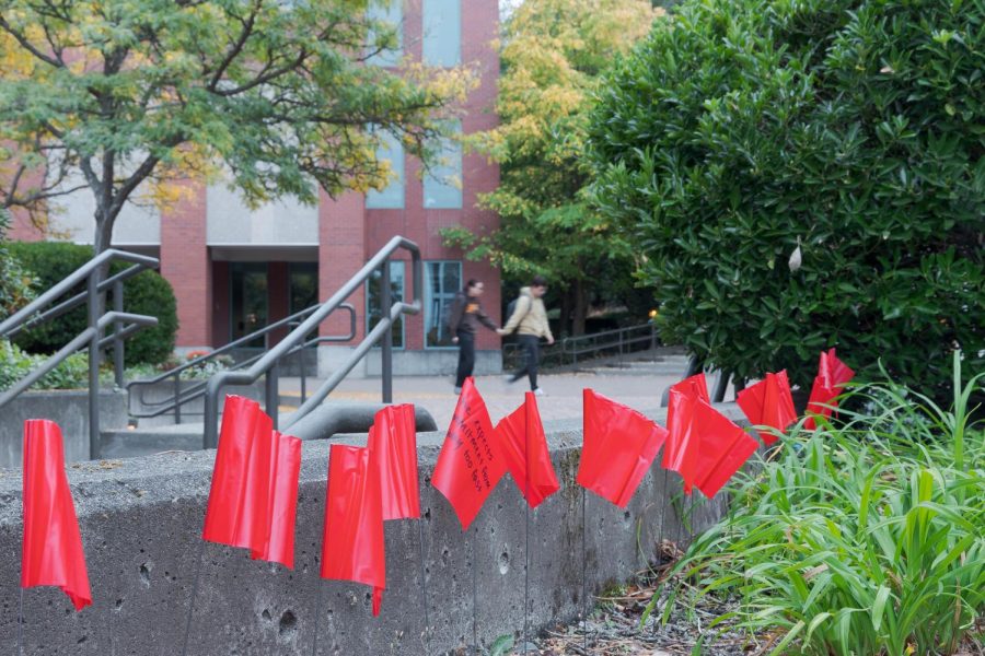 A couple holding hands walks through Martin Square in front of a row of red flags, one reading, She expects commitment from me way too fast on Wednesday, Oct. 5, 2022. The flags are part of a campaign raising awareness about and helping prevent stalking, dating violence, and sexual assault on college campuses.