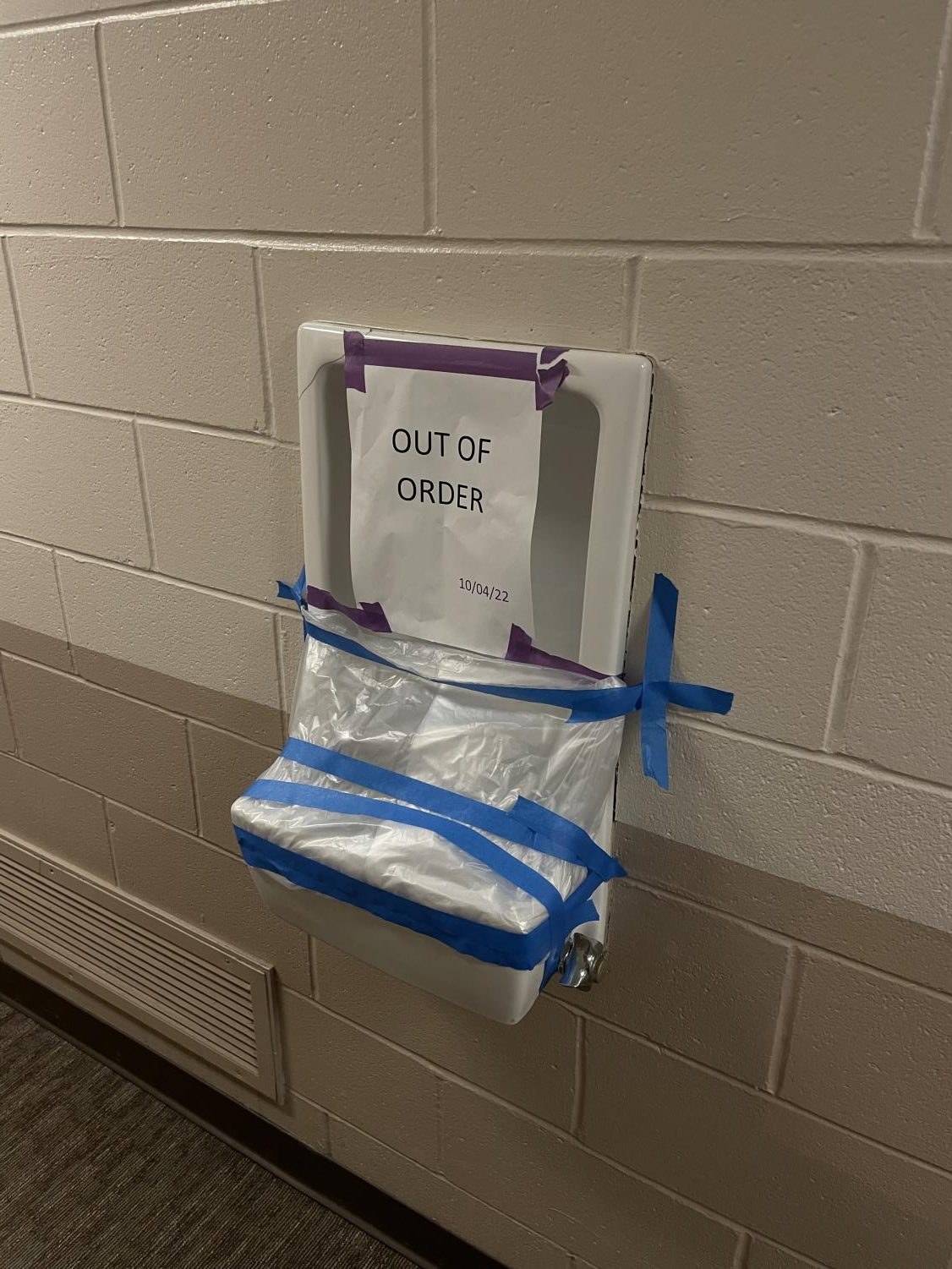 A broken water fountain on 5th East Ashton Hall With sign posted stating "Out Of Order 10/04/22" and plastic covering.