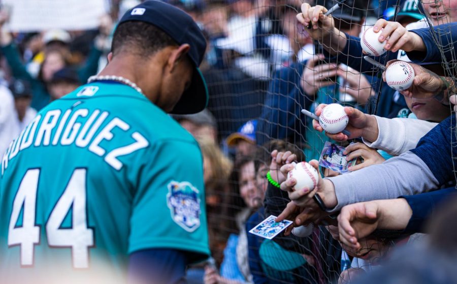 Fans reach through the foul ball netting offering baseballs and cards for Seattle Mariners center fielder Julio Rodriguez (44) to sign ahead of a baseball game Friday, April 14, 2023, in Seattle. The Mariners won 5-3.